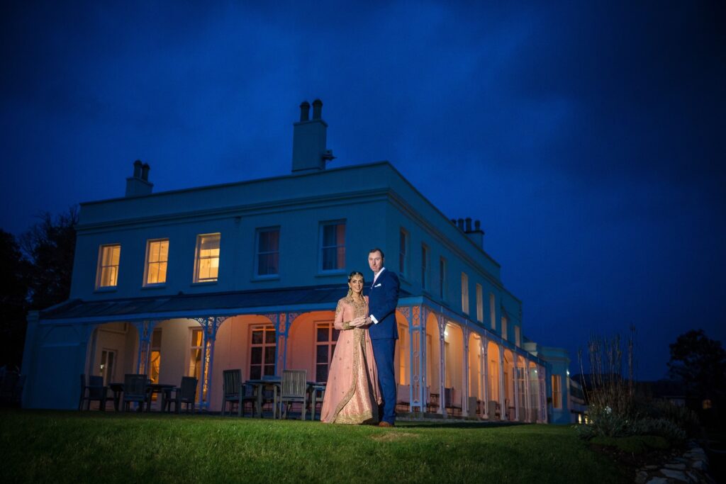 Bride and groom standing in front of Lympstone Manor in the evening