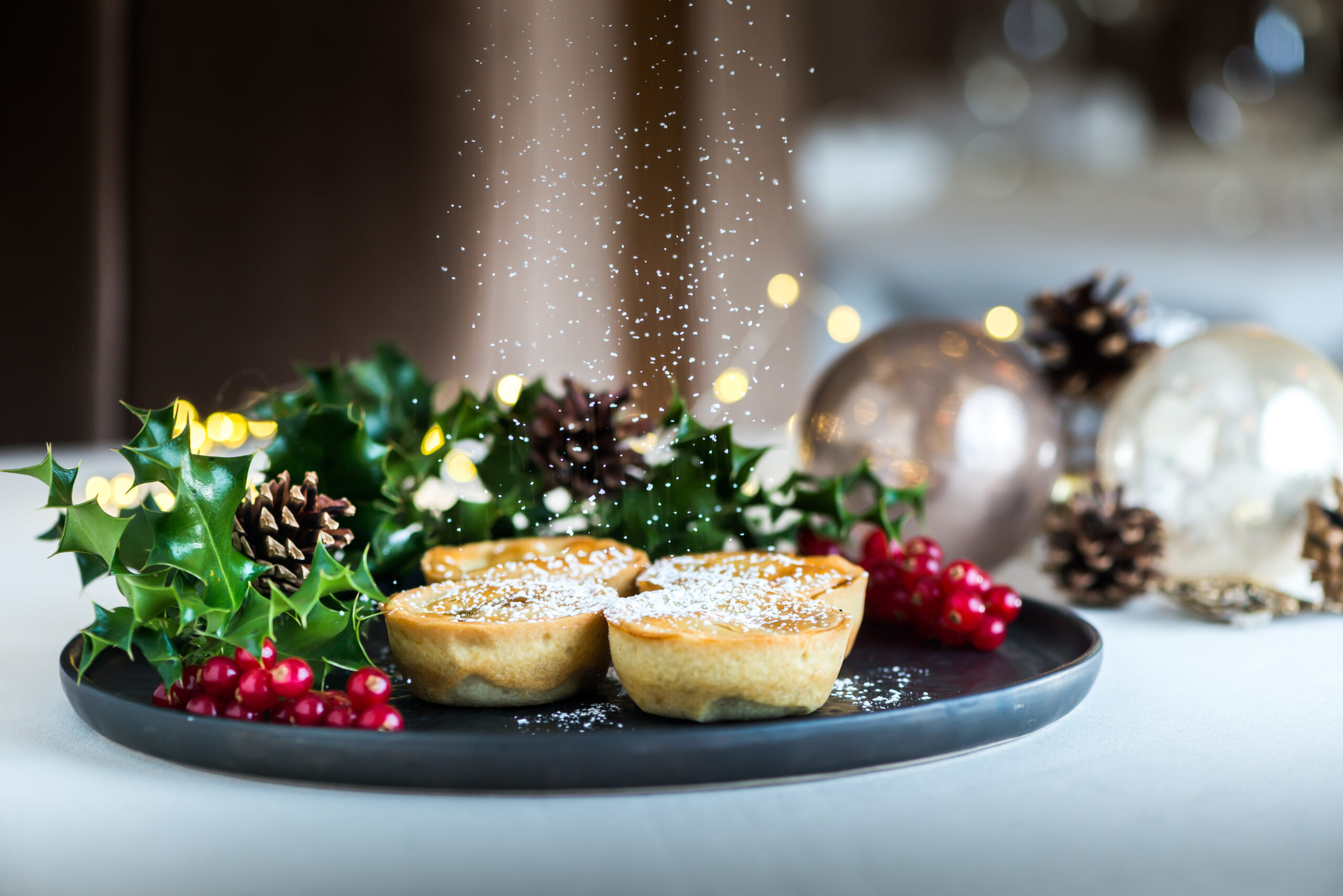 Mince pies displayed on a plate with holly and Christmas decorations